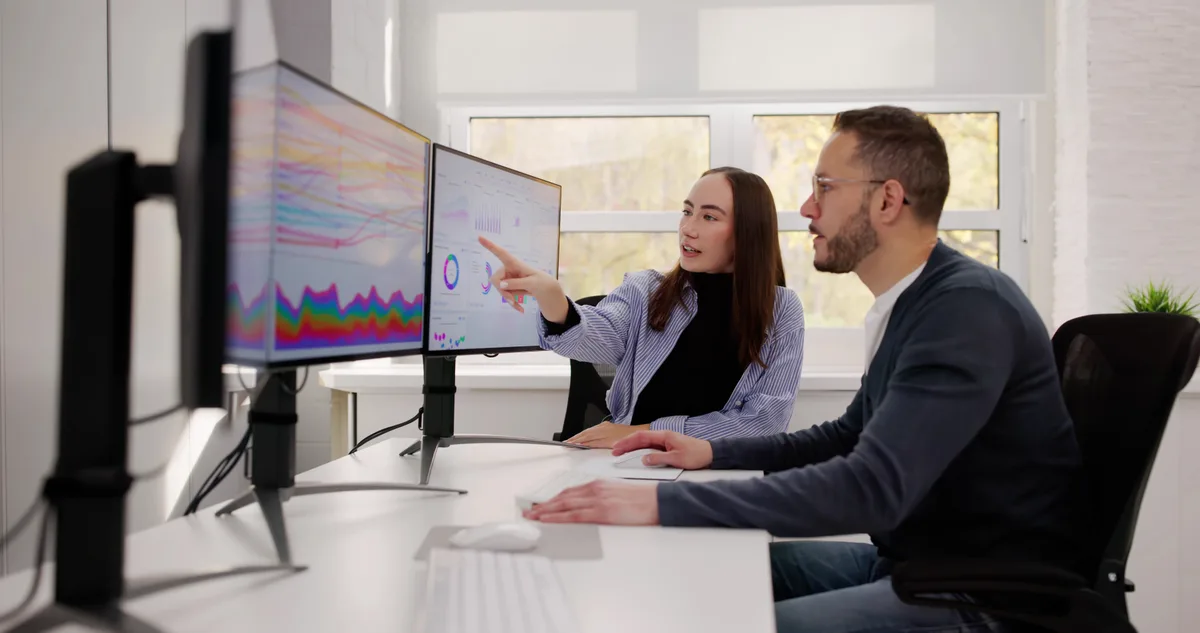 Two SEO specialists reviewing a website's organic traffic and ranking data on a monitor while planning a campaign handover