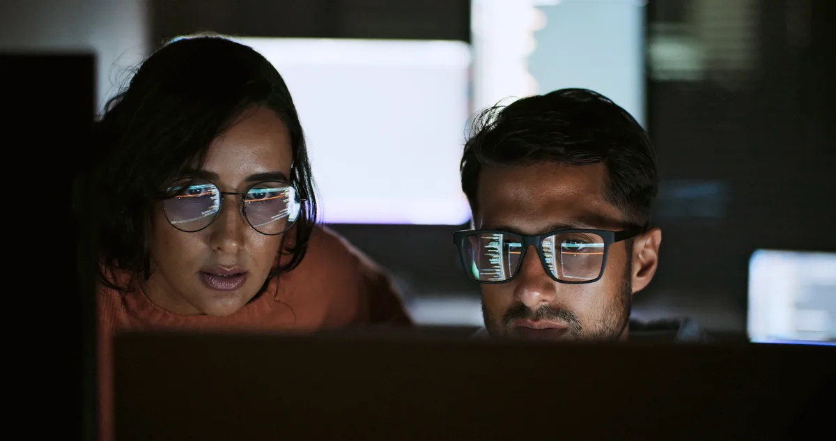 Two developers reviewing an inherited codebase together on a large monitor during a takeover audit
