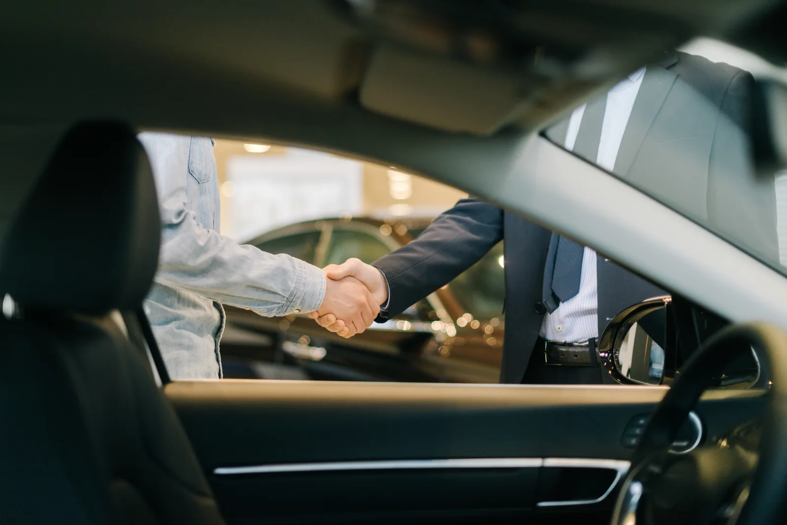 A buyer and salesperson shaking hands, seen through the open window of a new car