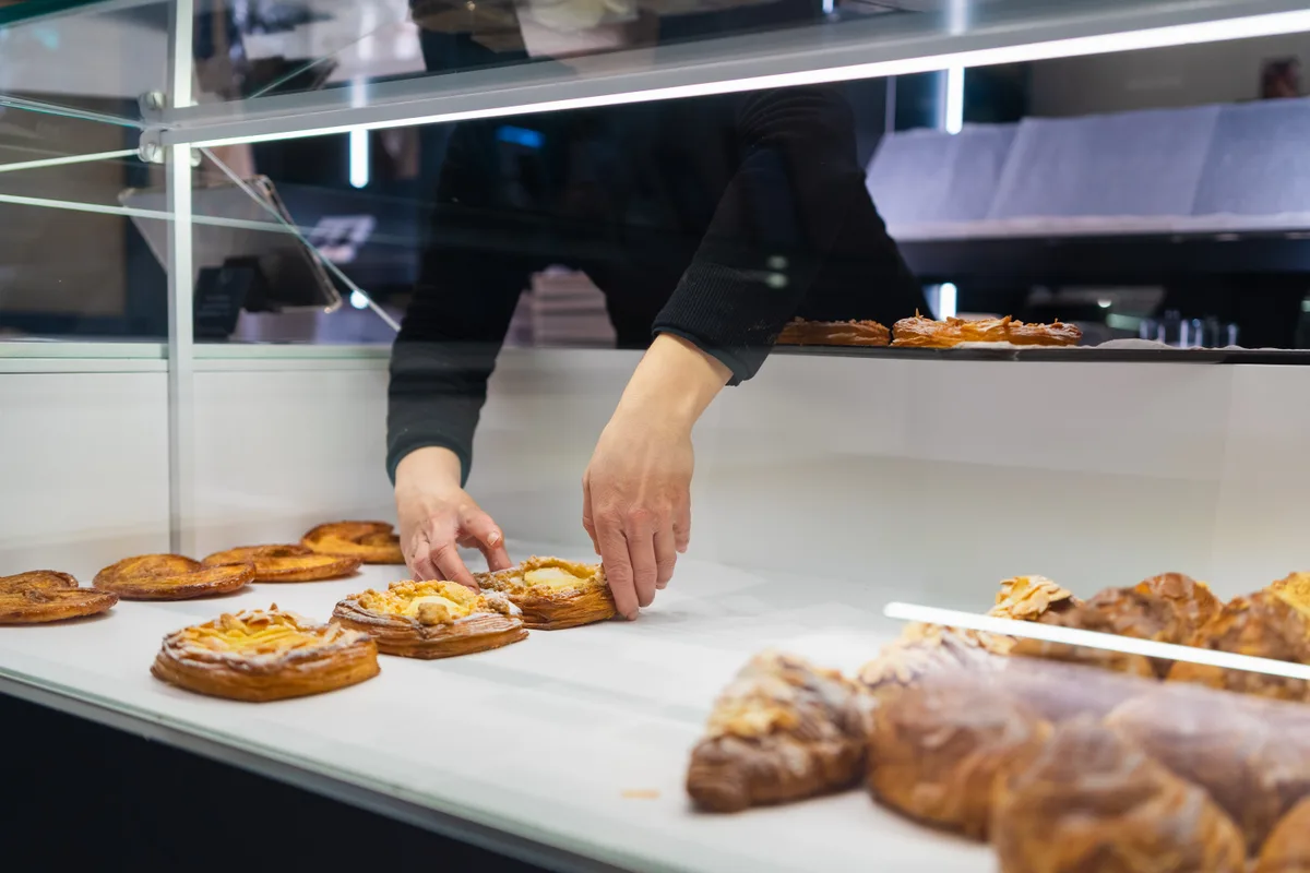 A baker arranging fresh croissants and pastries in a bakery display case