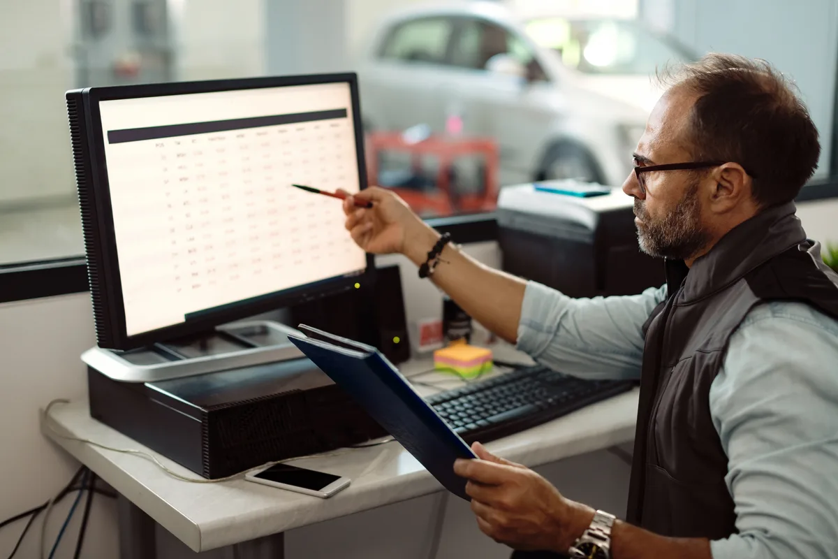 A dealership manager reviewing inventory and lead analytics on a computer in a showroom office