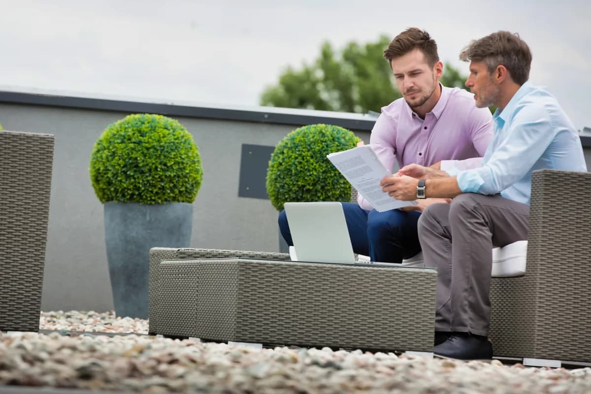 A landscaping company owner reviewing marketing performance on a laptop with a consultant beside a finished paver patio job