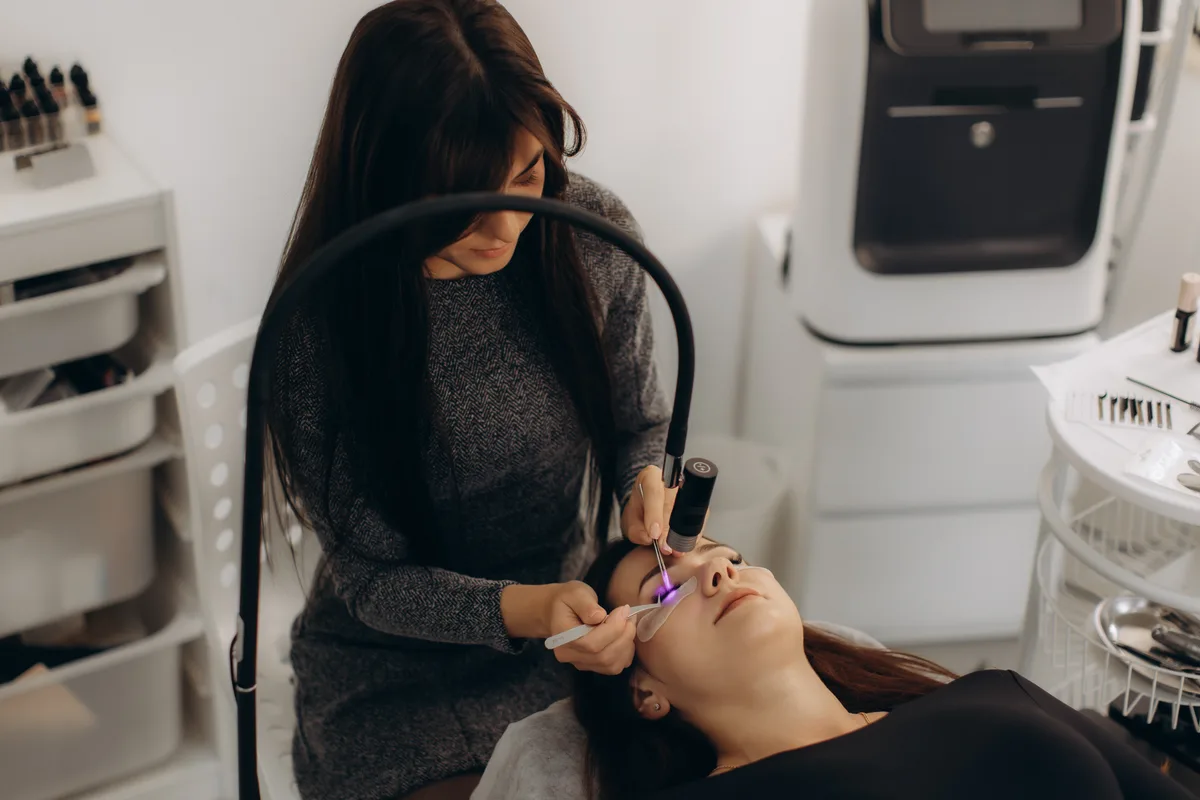 Lash technician applying eyelash extensions to a reclining client in a bright modern lash and brow studio
