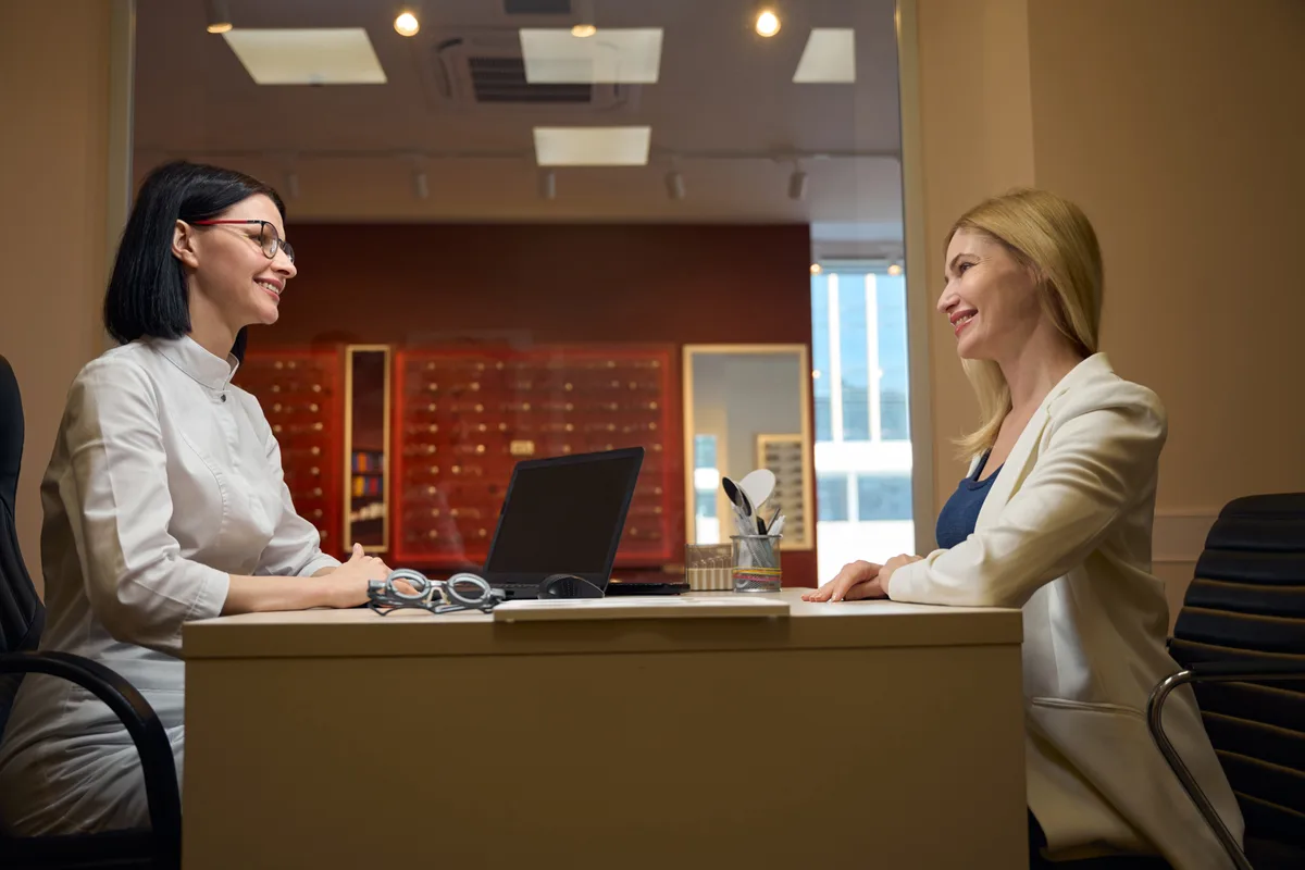 An optometry practice owner reviewing patient bookings at the front desk of a modern eye-care clinic