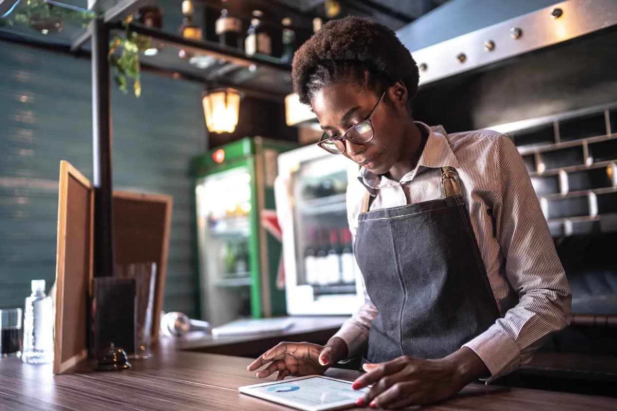 Restaurant owner reviewing reservation and marketing data on a tablet at the host stand