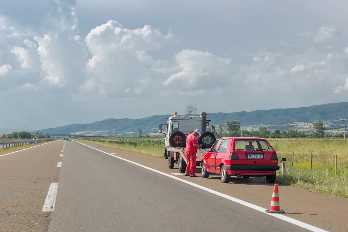 A tow truck operator winching a disabled car onto a flatbed at the side of a road