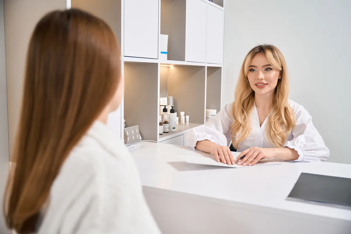 An esthetician greeting a client at the front desk of a clean, modern waxing studio