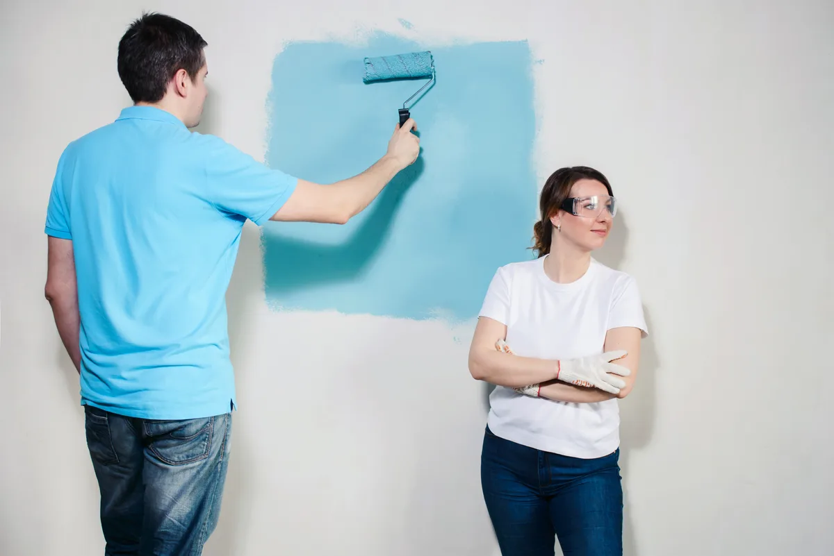 A professional painter rolling fresh paint onto an exterior house wall on a sunny day
