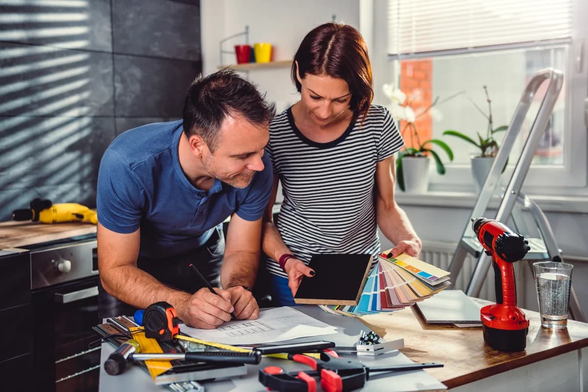 A remodeling contractor walking a homeowner couple through renovation plans at a kitchen counter