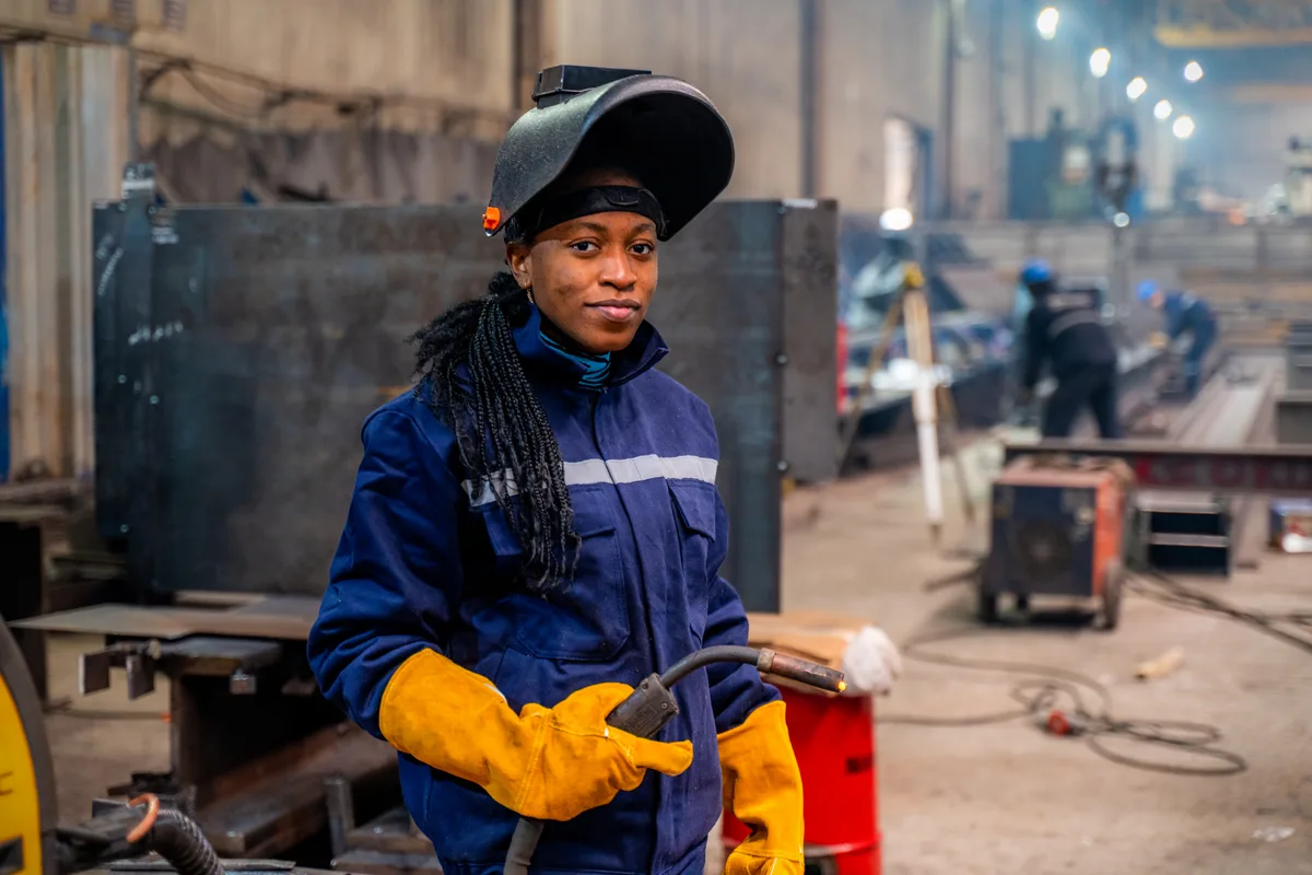 A welding student in protective gear practicing on a workbench inside a trade school training shop