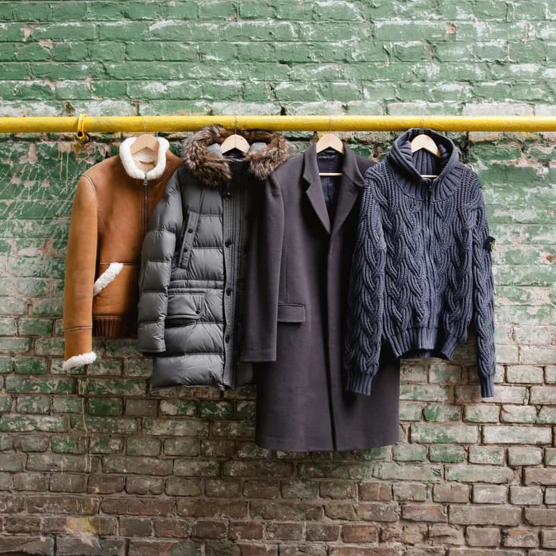 Heritage Overcoat and other outerwear hung on a steel rail against a brick wall