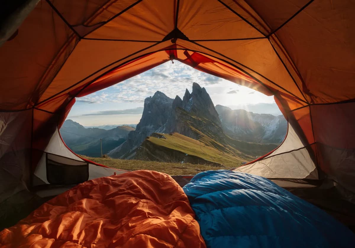Tent pitched on a ridge at dawn with mountain peaks behind