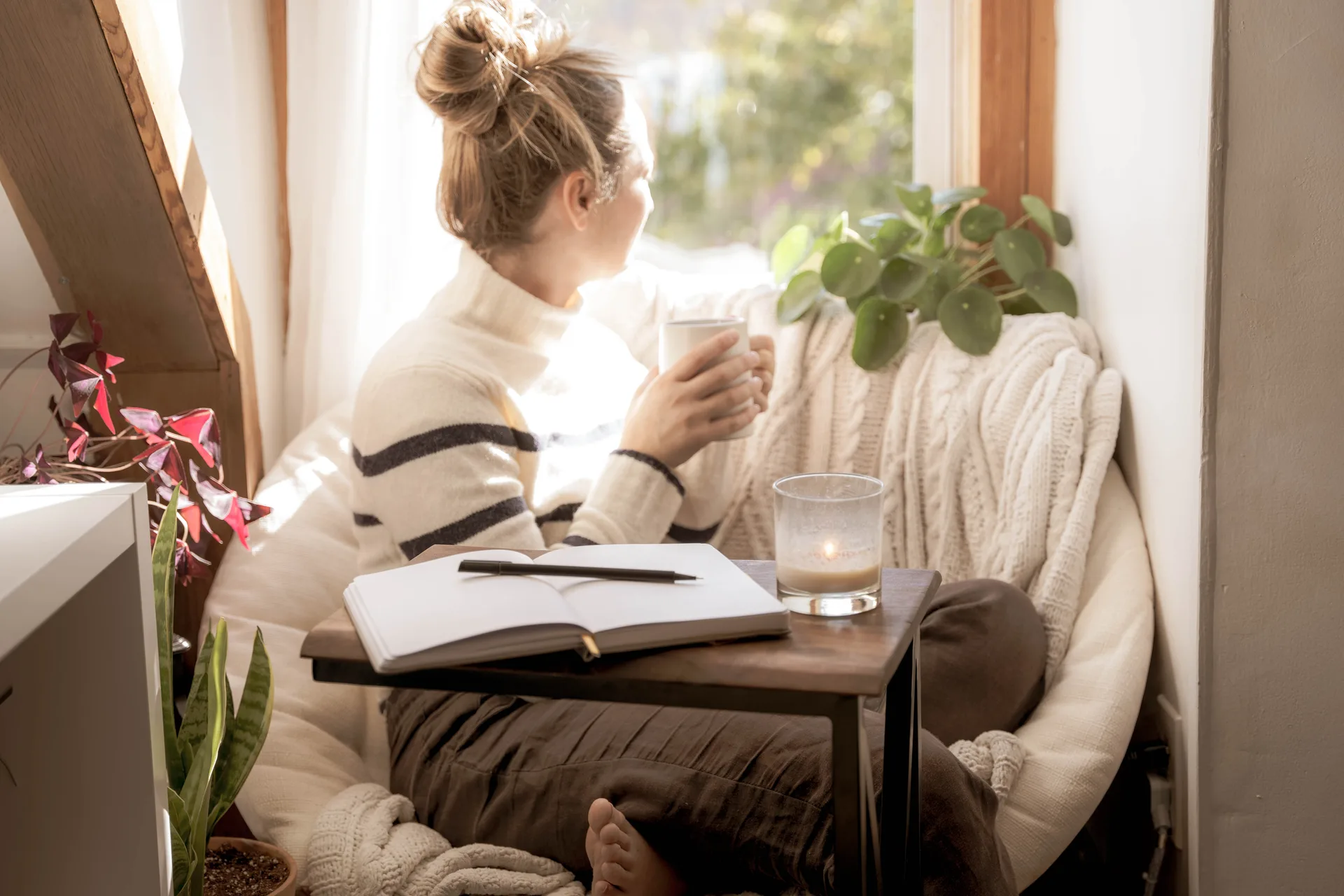 A woman with coffee writing in her journal by a bright window