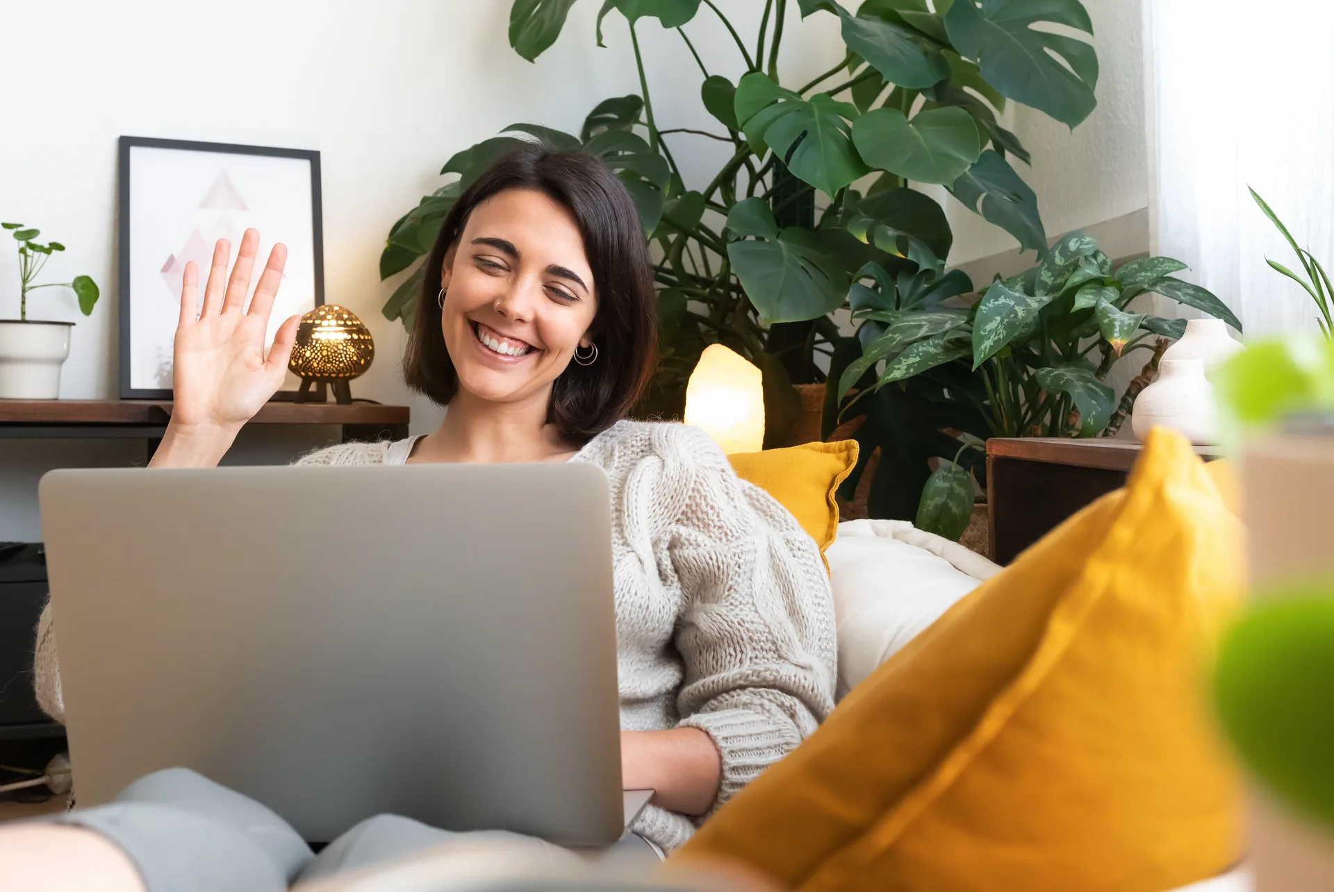 A woman on her couch waving hello to her therapist at the start of a video session