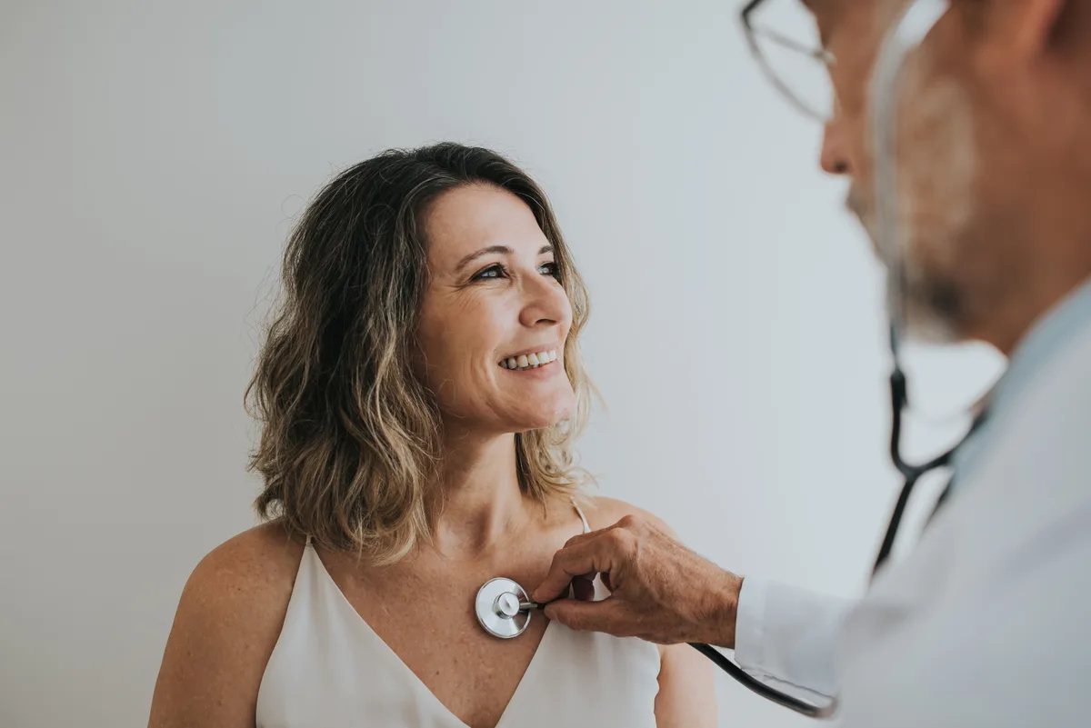 A patient in conversation with her cardiologist as he listens to her heart