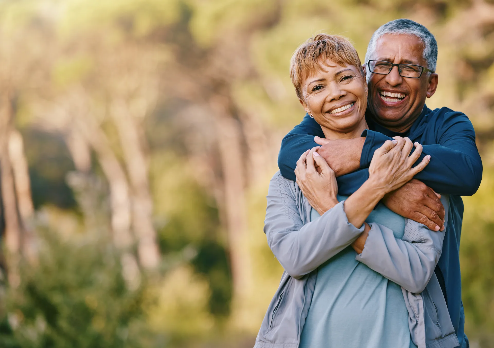 A senior couple smiling and embracing outdoors on a sunny day, dressed for a walk