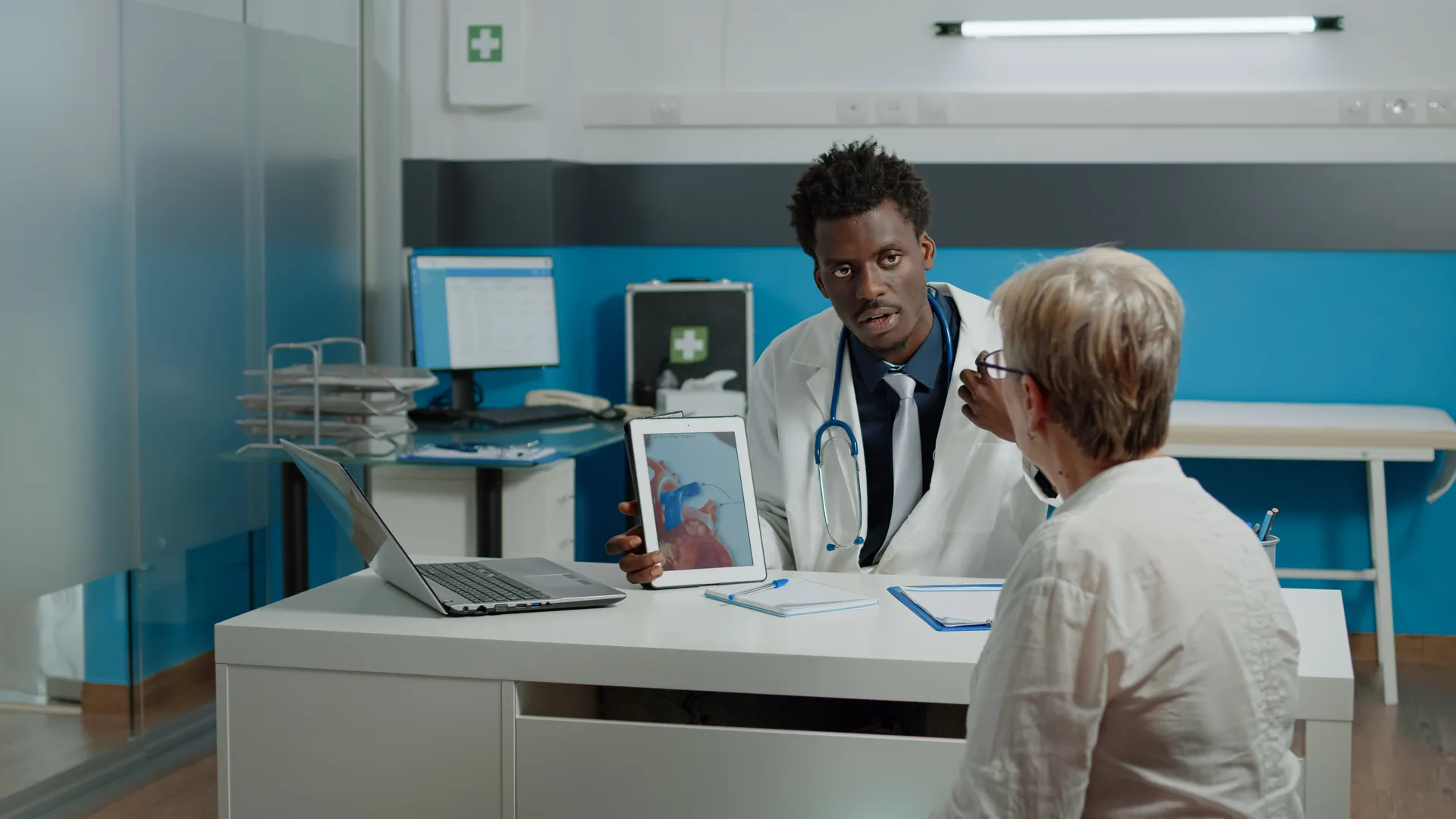 A physician reviewing imaging and notes on a tablet with a senior patient