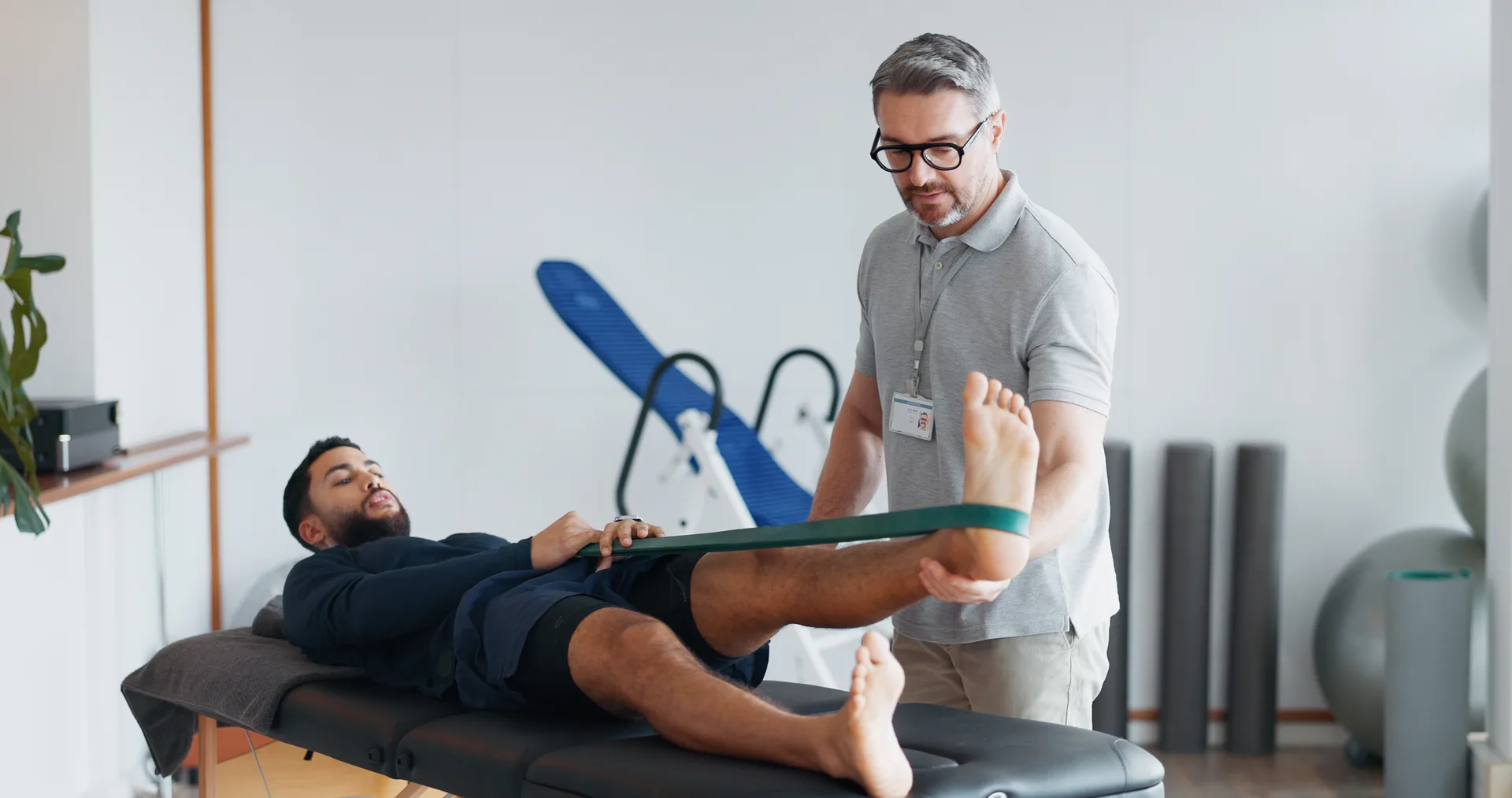 A physiotherapist stretching a patient's leg with a resistance band on a treatment table