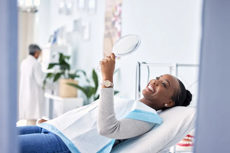 A patient admiring her smile in a hand mirror during her first visit