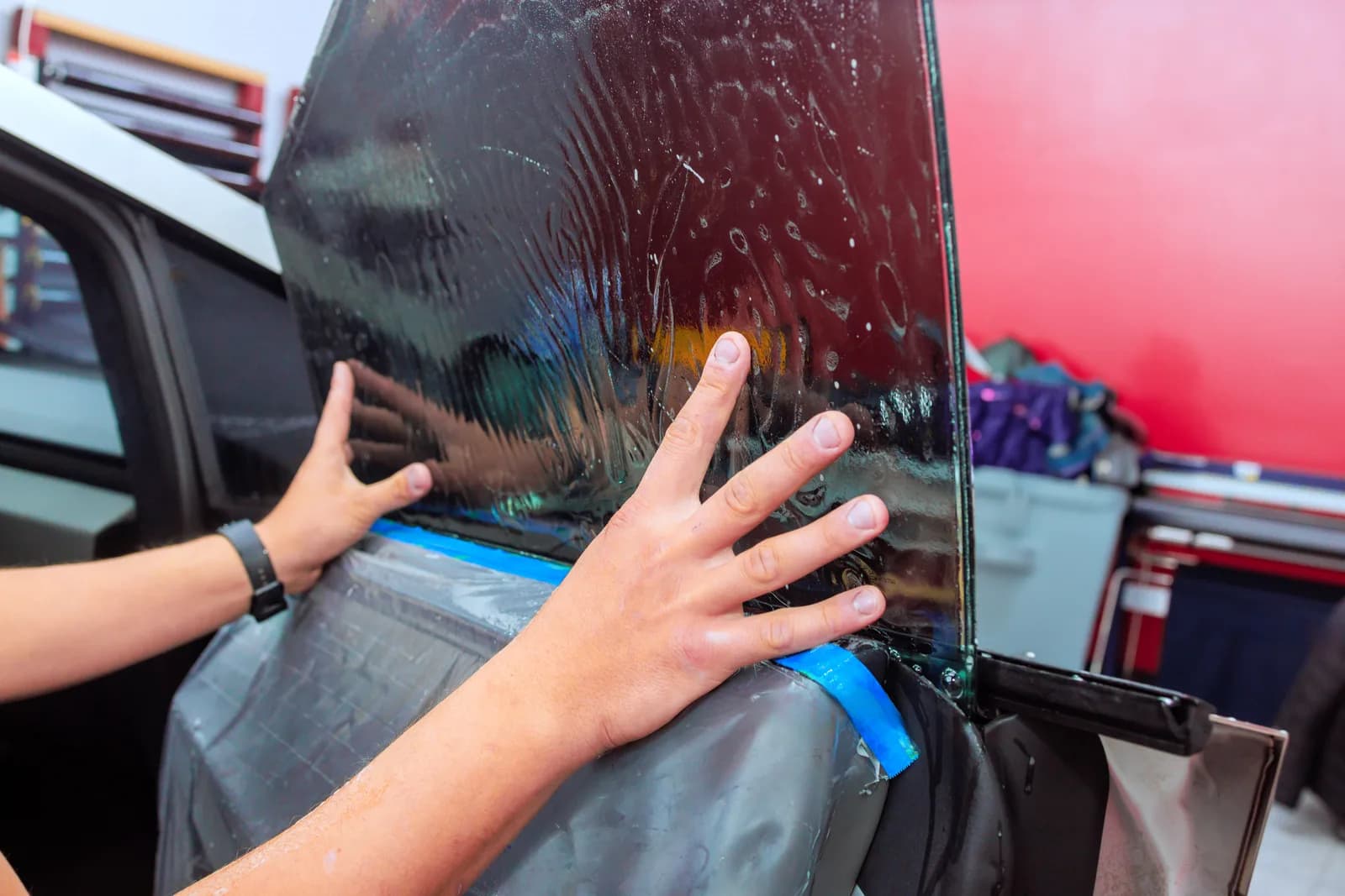 Installer applying tint film to a car window at an auto shop