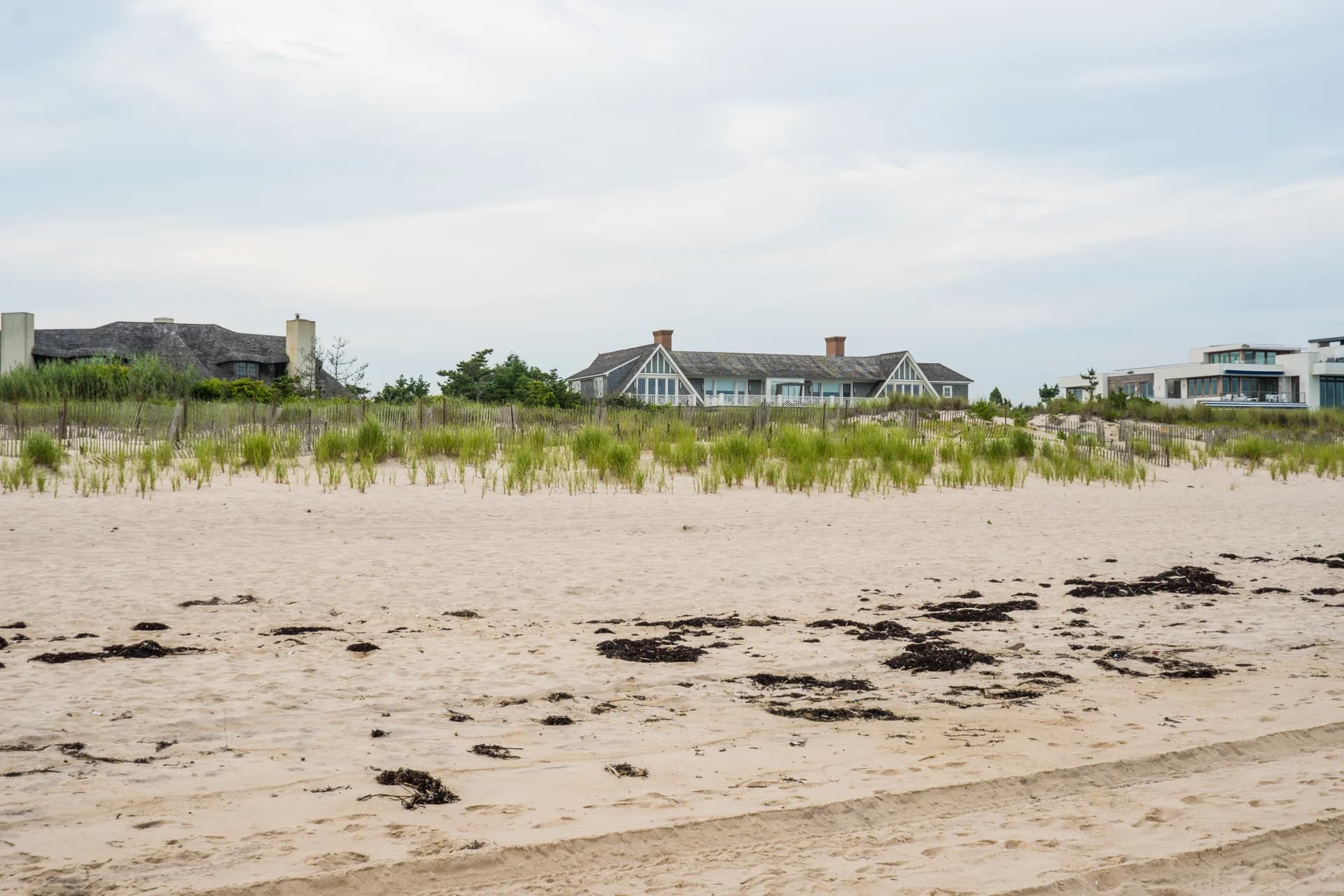 Hamptons oceanfront compound at golden hour, dune grass and cedar architecture.